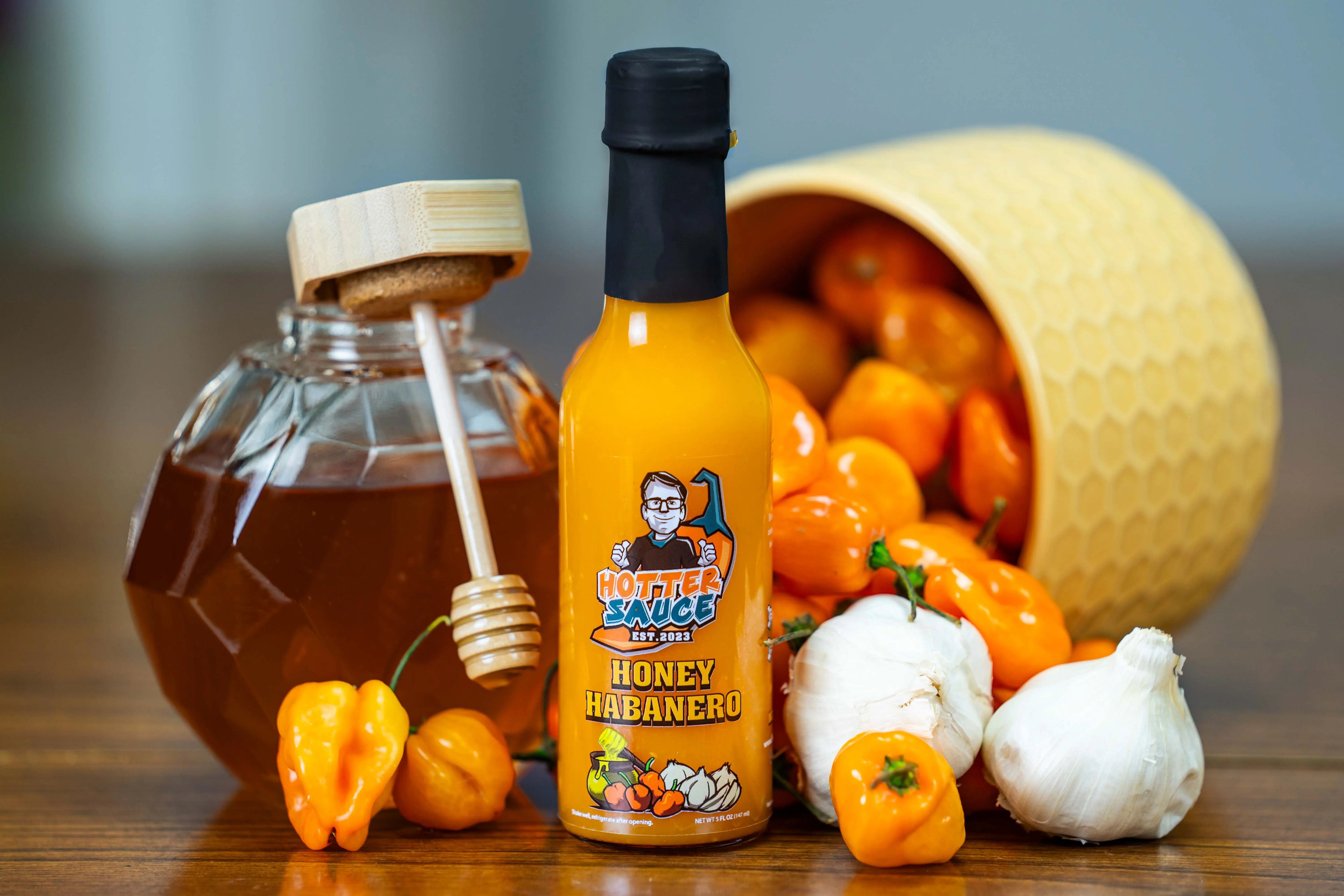 Bottle of Honey Badger Honey Habanero sauce with honey, peppers, and garlic on a wooden surface.