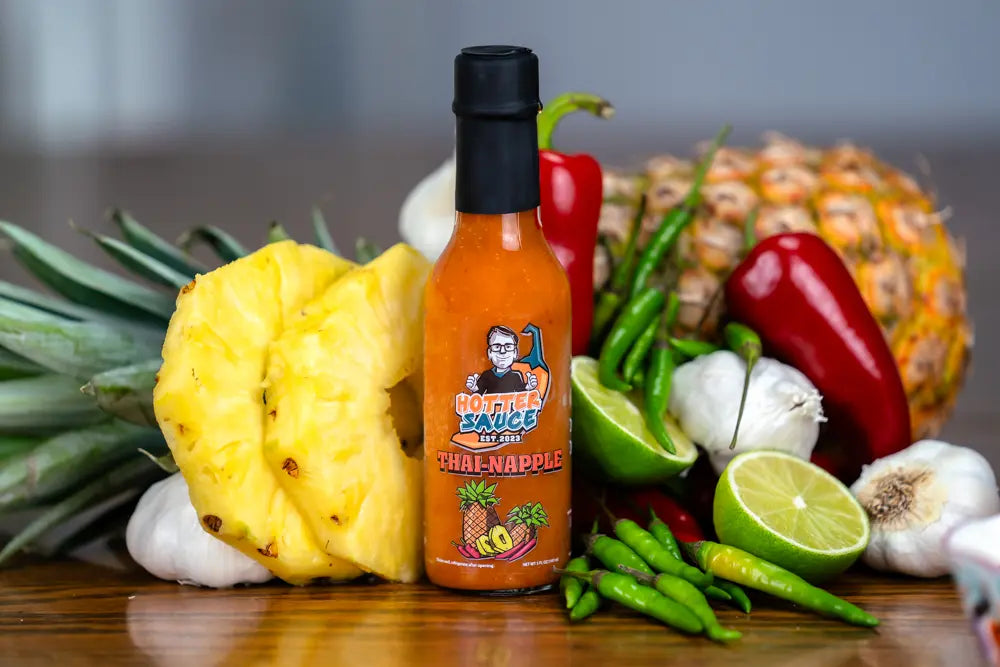 Hot sauce bottle labeled 'Thai Napple' with a pineapple, peppers, and garlic on a wooden surface.